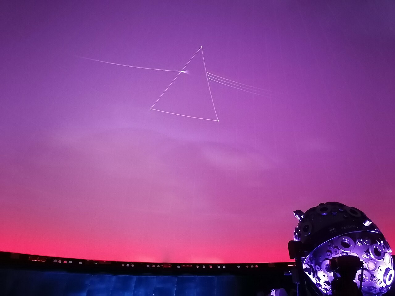 The prism of The Dark Side of the Moon projected on the dome of the Planetarium Hamburg, a beam of light entering from the left and a spectrum leaving on the right
